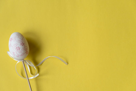 Easter white egg on a wooden stick, beautiful yellow background