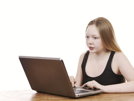 Beautiful young girl sitting by table using notebook computer - isolated on white background