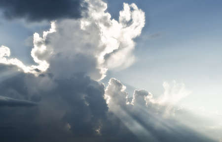 Beautiful cloudy blue sky scene with strong vibrant sun rays or beams shooting through the clouds.の写真素材