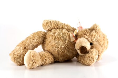 Cute furry brown teddy bear laying down sick holding his head isolated on white background with copy space の写真素材