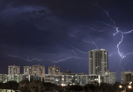 Urban city night scene with large lightning bolt lighting up the cloudy stormy sky 