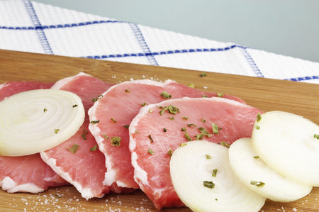 Juicy raw pork loin chops with onion slices and spices on wooden cutting board with copy space 
