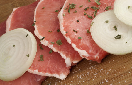 Juicy raw pork loin chops with onion slices and spices on wooden cutting board with copy space の写真素材