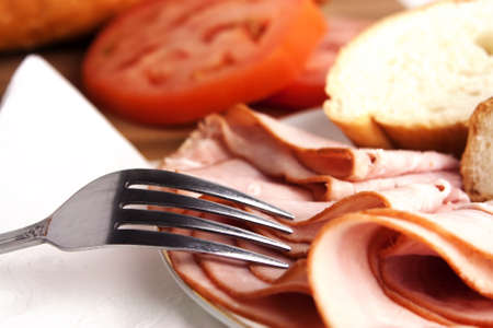 Delicious lunch time spread with ham, bread, cheese and tomatoes with silver forkの写真素材