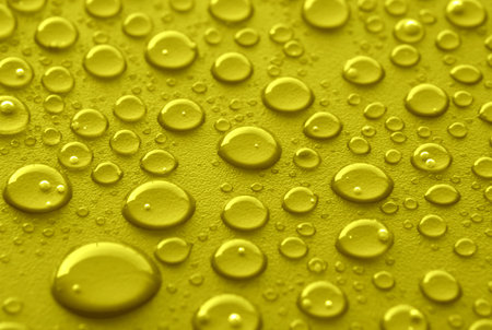 Shiny water drops sprayed on textured yellow or gold surface.の写真素材
