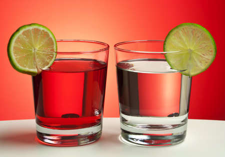 Two red drinks with lime slices on white table with red gradient backdrop.の写真素材