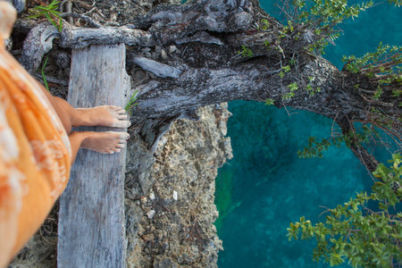 Highly Detailed Photo Woman Legs. Girl Looking Down Cliff Old Tree. Blue Ocean Water Blurred...