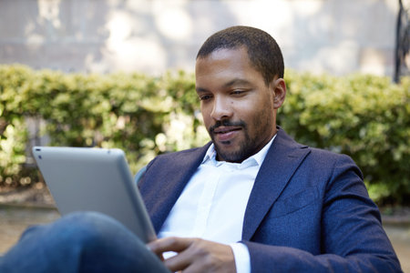 Young american african businessman in informal clothes working at sunny street on electronic touch...