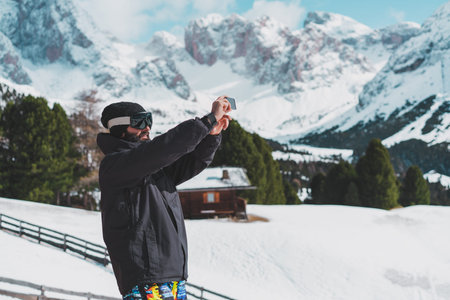 Bearded young snowboarded in sunglass mask, at the ski resort on the background of mountains and...