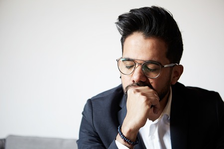 Portrait of handsome bearded man taking rest at home. Young handsome man wearing glasses thinking with close eyes against empty white wall in the backgroundの写真素材