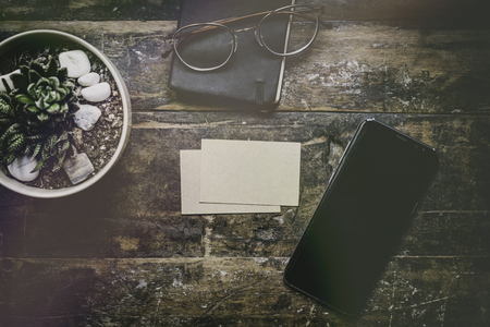 Mock-up of two blank craft business cards, smartphone and cactus on natural brown authentic wooden desk. Business empty mock-up background for message writing.Business accessories conceptの写真素材