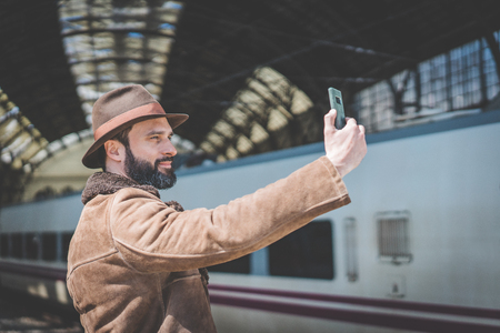 Handsome businessman making selfie on a mobile phone.Casual professional entrepreneur using smartphone outside while waiting train on railway stationの写真素材