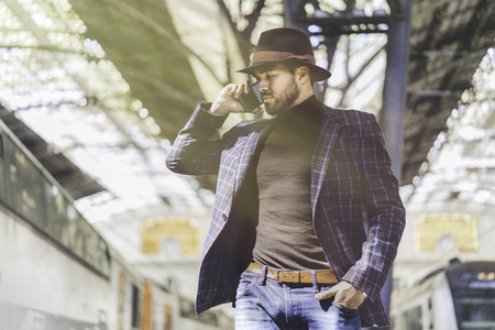Confident young hispanic businessman holding smart phone in his hand and calling while he standing at the railway platform waiting for the train.の写真素材