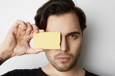 Young man holding empty yellow color credit card front of male face on blank white background. Business mock-up background for message writing. Horizontal Mockup.の写真素材