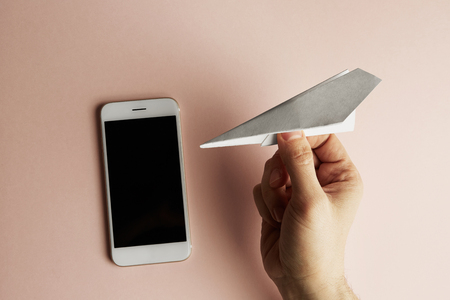 Smartphone with Flat lay of white paper plane in male hand on pastel pink color background.Concept Horizontalの写真素材