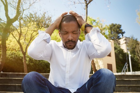 Young american african businessman in informal clothes put his hands on his head and taking a deep breath outside corporate office.Business yoga and stress free environment.Peace of mind conceptの写真素材