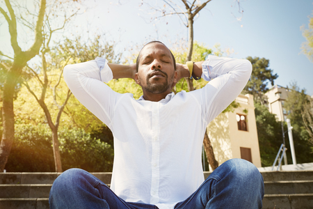 Young american african businessman in white shirt put his hands on his head and taking a deep breath outside corporate office.Business yoga and stress free environment.Peace of mind conceptの写真素材