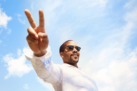 Smiling confident young African-American man hipster in white shirt spending time at outdoor.Blue sky with clouds on backgroundの写真素材