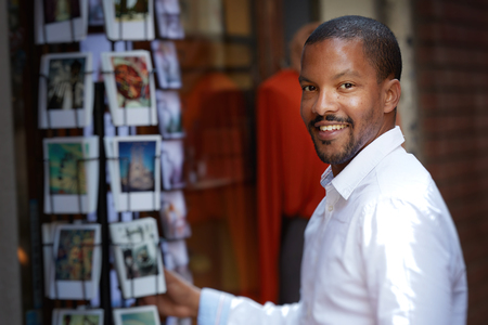 Handsome young African man in white shirt looking at camera and chooses postcardの写真素材
