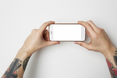 Male tattoo hand holding cell phone with empty screen on white backgroundの写真素材