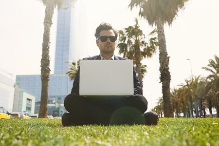 Young caucasian businessman in formal clothes working at sunny day on green grass on laptop. Blurred backgroundの写真素材
