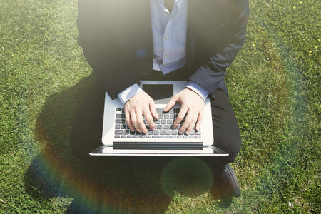 Working outside office.Young businessman in formalwear typing on laptop while sitting at city green...
