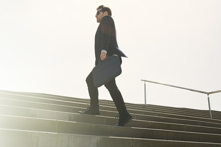 Young confidental businessman wearing suit and running fast upstairs. Horizontal outdoors shot.の写真素材