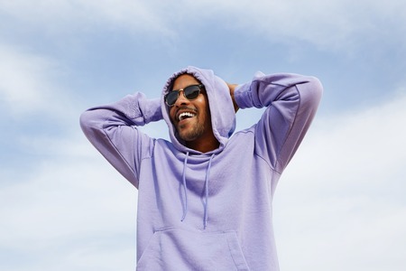 Summer active sports concept. Smiling happy young African-American man hipster in sport hoody and sun glasses on the beachの写真素材
