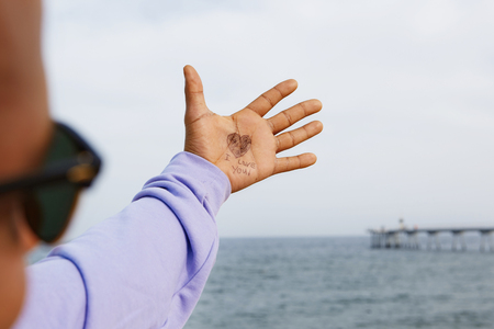 African-American hipster wearing hoody writed love romantic message on his hand at the sunny beachの写真素材