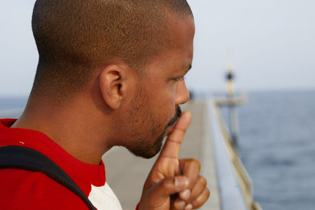 Close up portrait of handsome cheerful silent american african man making hush gesture at the beach