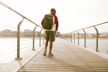 Active African-American hipster traveler wearing backpack and walking on the beach and enjoying sea viewの写真素材