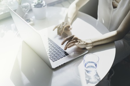 Beautiful woman working on a laptop sitting at the table in living room of modern house.の写真素材