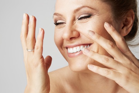 Beautiful smiling woman with clean skin, natural make-up, and white teeth on gray background. Close up portrait.Medical and cosmetic facial skin healthcare conceptの写真素材