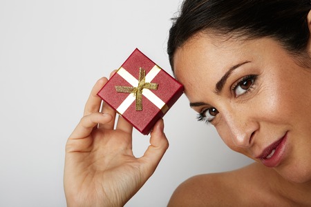 Fashion photo of a beautiful brunette woman with dark short hair holding hand gift box over white empty background.Positive human emotions, reaction, gestures.Copy paste space text messageの写真素材