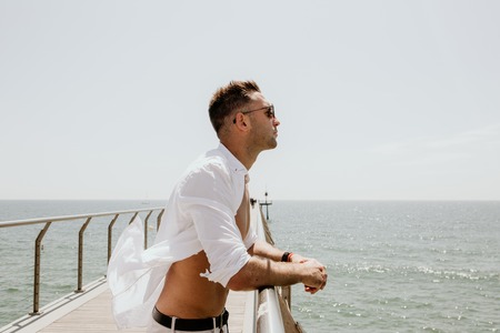 Handsome happy man wearing white shirt and sunglasses at the sea or the ocean background.Travel vacation holiday conceptの写真素材
