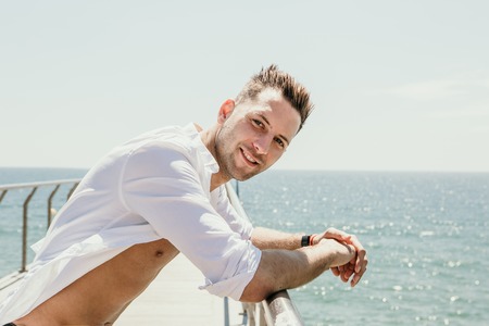 Handsome happy smiling young man wearing white shirt at the sea or the ocean background.Travel vacation holiday conceptの写真素材