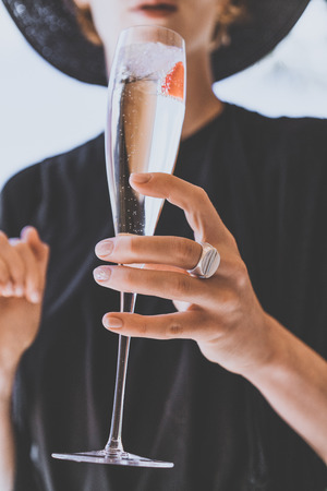 Fashion female woman model holding hand glasses champagne with strawberry inside on sunny terrace overlooking swimming pool at summer day outside of the city.Beauty holidays concept.Verticalの写真素材