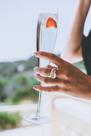 Female woman holding hand glasses champagne with strawberry inside on sunny terrace overlooking swimming pool at summer day outside of the city.Beauty holidays fashion concept.Verticalの写真素材