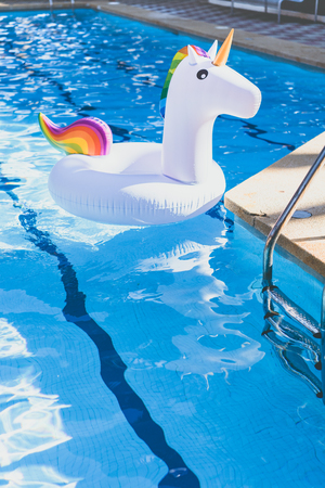 Inflatable colorful white unicorn at the swimming pool. Vacation time in the swim pool with plastic toys. Relaxation and fun concept. Ripple Water in swimming pool with sun reflection. Verticalの写真素材