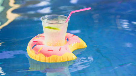 Fresh cocktail with ice and tasty limon floating on an inflatable toy pink donut toy at swimming pool.Vacation and relaxation time in swim pool at summer dayの写真素材