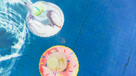 Two fresh cocktails with ice and tasty limon floating on an inflatable toys white flamingo and pink donut toy at swimming pool.Vacation and relaxation time in swim pool at summer dayの写真素材