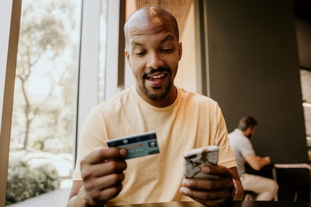 Happy Black african man holding hands credit card and mobile phone. Technology, internet banking, e-commerce and online trading conceptの写真素材