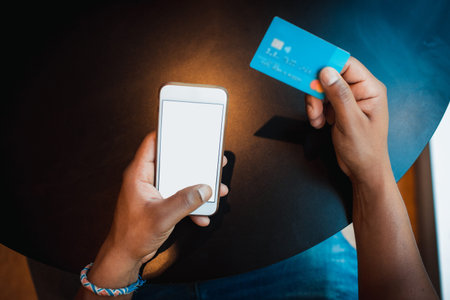 Closeup view of male hands touching mobile phone.African man using smartphone and credit card while...