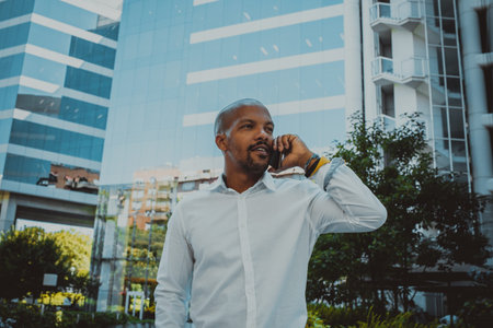 Positive african american male using smartphone outdoor. Office skyscrapers in the background