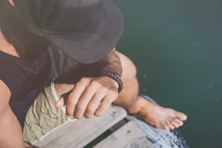 Bearded man model wearing black cap and tshirt looks away, sunset in the sea scenery.