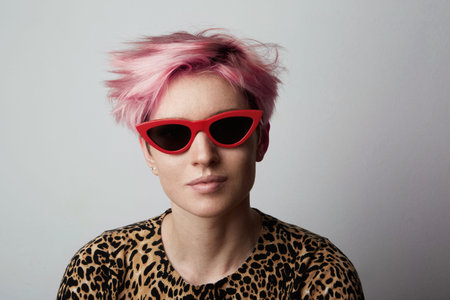Fashion Portrait of young Fabulous trendy woman with red sunglasses and pink short hair poising at...