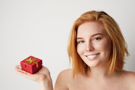 Beauty redhead woman holding hand red gift box over white empty backgroundの写真素材