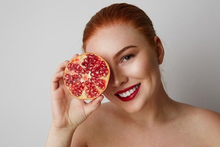 Beauty woman with orange pomegranate cut in half over white background. Attractive fresh vitamin conceptの写真素材
