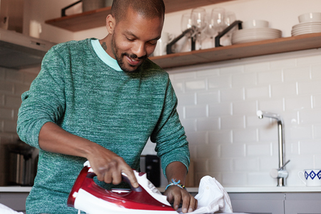 Attractive american black man is ironing white shirt at home.の写真素材