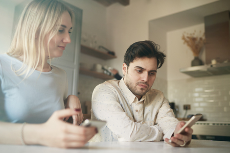 Attractive hispanic man and blonde woman using mobile phones at homeの写真素材